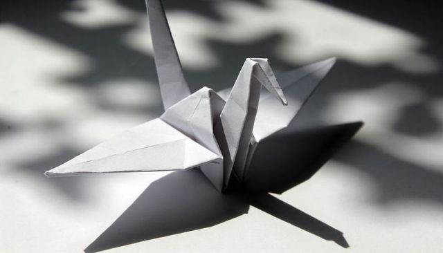 Sunlit origami crane casting long shadow with dappled leaf silhouettes