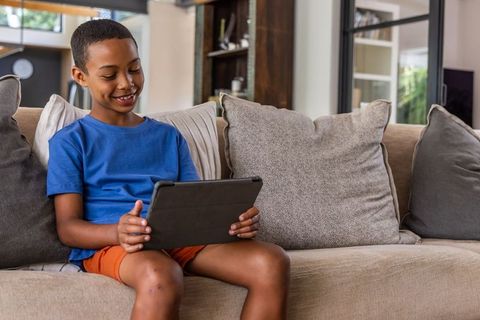 Smiling african american boy using tablet on sofa at home for learning and play