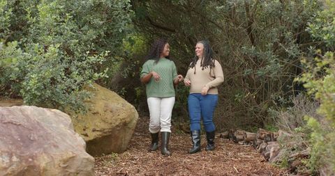 Two women walking and chatting on woodland trail, sweaters and boots, autumn companionship