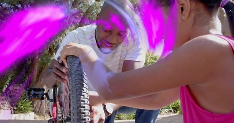 Parent teaching child bicycle repair on driveway, kneeling and fixing wheel with teamwork