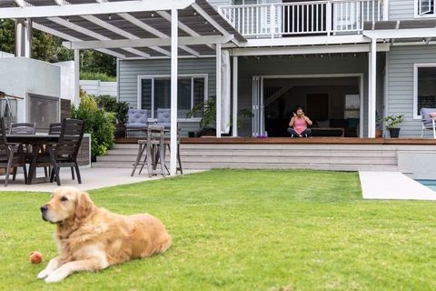Mature woman talking on phone on deck with golden retriever relaxing on green lawn