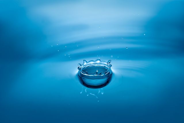 This image of a water droplet splash capturing ripples on a blue surface is ideal for themes involving purity, cleanliness, and fluidity. It works well for advertisements, backgrounds, and designs related to water conservation, health, and liquid products. The calm and serene nature of the splash can symbolize tranquility and freshness.