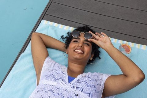 Indian woman relaxing poolside on light blue towel wearing white lace cover-up and sunglasses