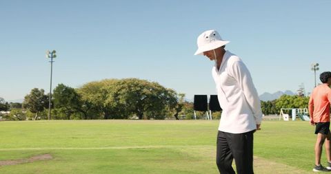 Profile man standing on sports field wearing white bucket hat and casual athletic clothing