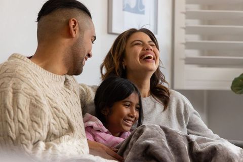 Cozy diverse family laughing together on sofa wrapped in blanket, home comfort lifestyle