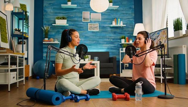 Recording fitness podcast with two cohosts on yoga mats using microphones and headphones