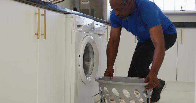 Middle-aged African American man performing household chore of doing laundry. Suiting articles on everyday life, domestic responsibilities, home care guides, and balanced lifestyles. Excellent visual for home appliance ads, domestic help blogs, and lifestyle promotion.