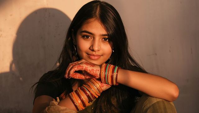 Sunlit indian woman with henna and colorful bangles resting chin in golden hour portrait