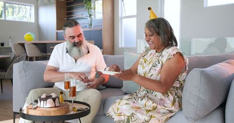 Senior couple celebrating with cake and drinks on sofa