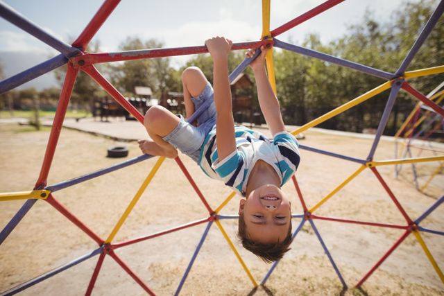 Portrait of happy schoolboy playing on dome climber at school playground