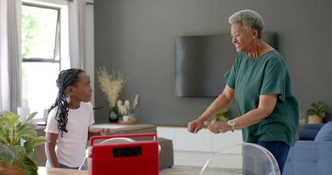African american grandmother dancing with granddaughter beside red radio in living room