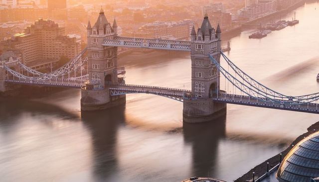 Aerial tower bridge bathing in golden hour light over river thames with city hall dome