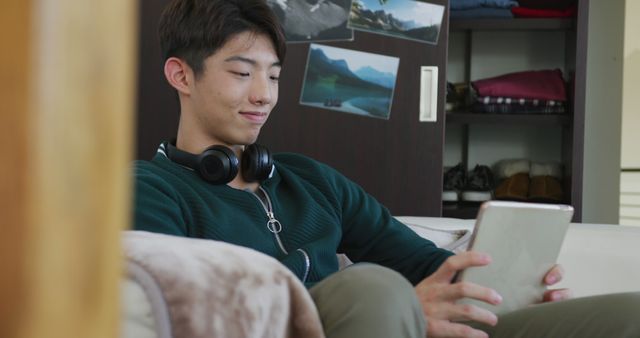 Asian boy using digital tablet sitting on the couch at home. teenager lifestyle and living concept