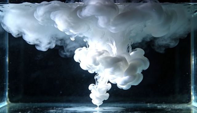 Descending white ink plume forming billowy cloud in water tank for abstract background