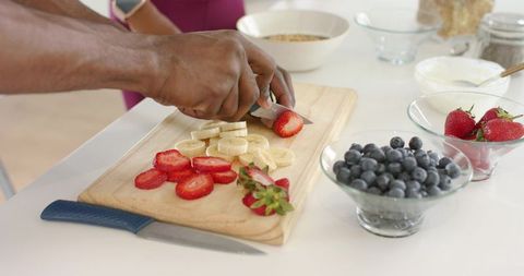 African american couple preparing healthy breakfast bowls slicing strawberries and bananas