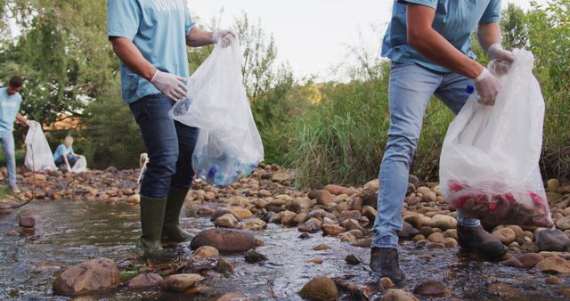 Volunteers actively collecting trash along a river, wearing gloves and holding bags for garbage. Suitable for use in articles or campaigns related to environmental conservation, community service projects, and eco-friendly initiatives. Highlights teamwork and the importance of maintaining clean natural spaces.