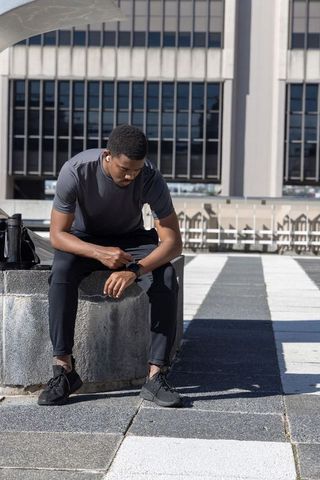 African american man checking smartwatch on rooftop after urban workout with earbuds