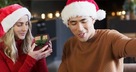 Couple celebrating holiday morning exchanging gift in cozy living room with santa hats