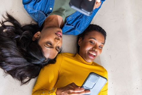 Multicultural friends lying on floor scrolling smartphones together casual lifestyle