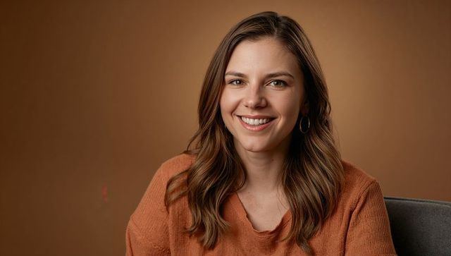 Smiling professional woman wearing rust sweater with hoop earrings warm brown backdrop