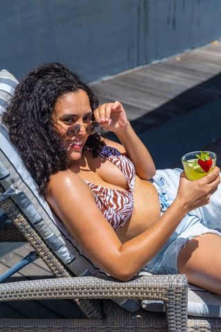 African american woman lounging in zebra bikini on sunlounger sipping strawberry cocktail