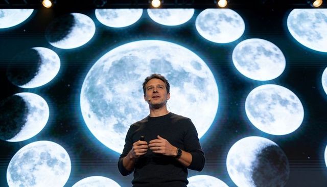 Male speaker presenting lunar ai concept on stage with large moon projection backdrop