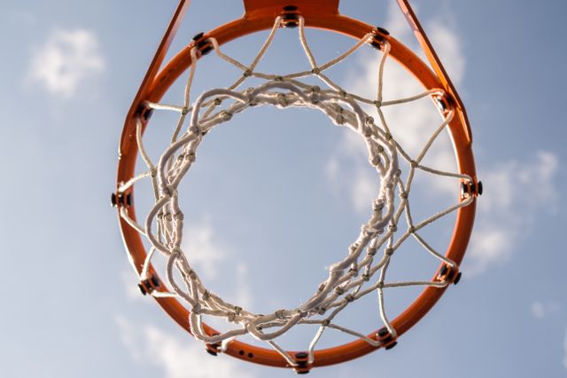 Basketball hoop with net viewed from below against blue sky and clouds. Useful for sports themes, outdoor activity promotions, fitness graphics, recreational concepts, and motivational posters highlighting sports spirit and energy.