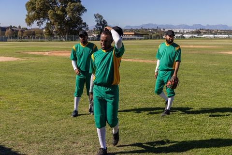 Baseball outfield trio walking across sunny suburban field player adjusting cap
