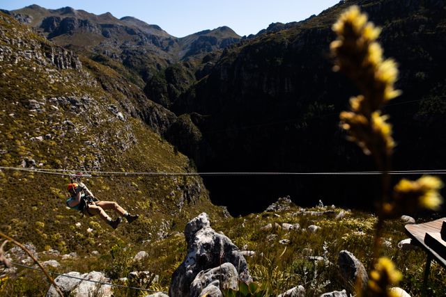 This image captures a man enjoying an adventurous zip lining experience through a mountainous landscape on a sunny day. Ideal for use in travel brochures, adventure tourism websites, outdoor activity promotions, and vacation planning materials. It conveys excitement, thrill, and the beauty of nature.