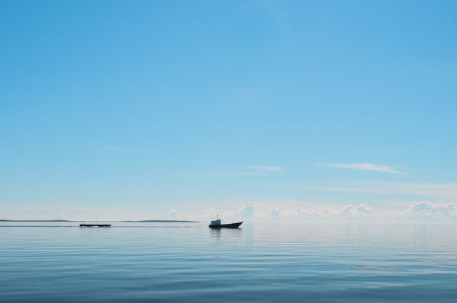 Depicts tranquil maritime scene with boats on expansive calm sea under clear blue sky. Perfect for websites or publications focused on travel, marine life, tranquility, relaxation, or oceanography.