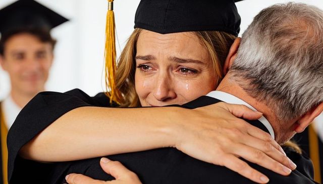 Emotional female graduate hugging father with tears during college graduation ceremony