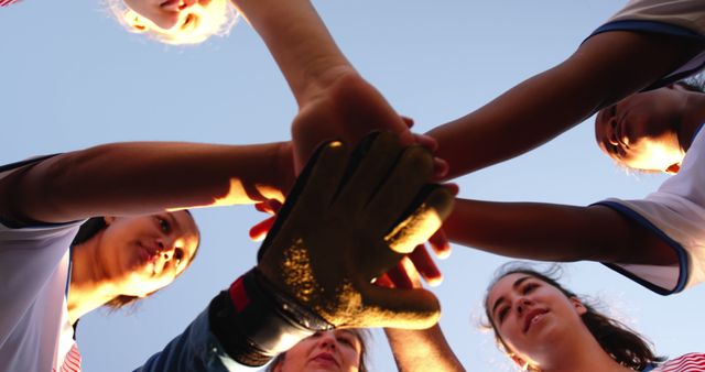 View from below of diverse female football team stacking hands in court on sunny sports field. Active lifestyle, sport, competition, hobby and wellbeing, teamwork, unaltered.