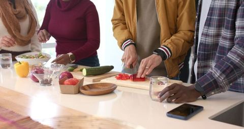Multicultural friends chopping vegetables at modern kitchen island preparing healthy meal