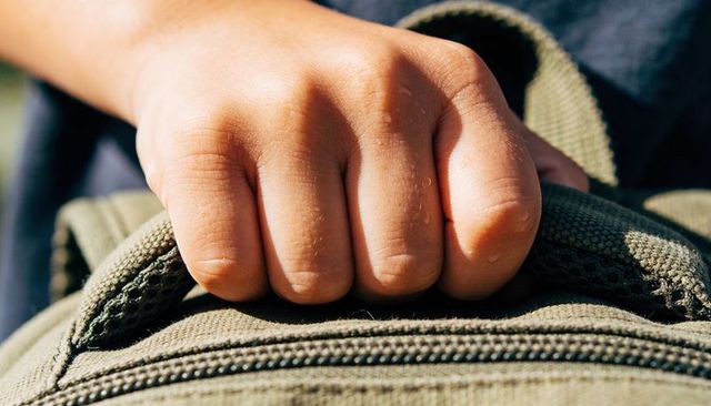 Child hand holding olive green backpack handle close-up with water droplets and texture