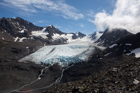 Blue Glacier Flowing Through Rugged Alpine Valley With Snow-Capped Peaks and Clouds