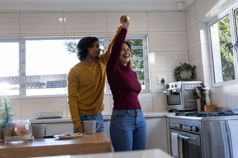 Diverse couple twirling in cozy morning kitchen, dancing and laughing over breakfast