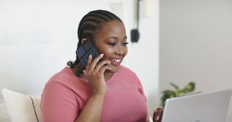 African american woman working remotely on laptop while talking on smartphone