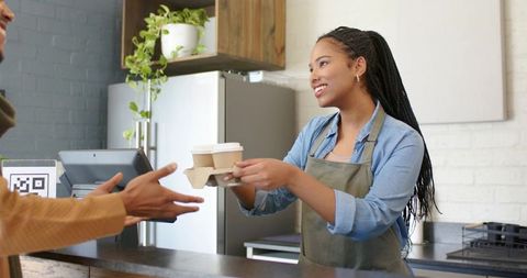 Smiling barista handing takeaway coffee cups to african-american customer at cafe counter