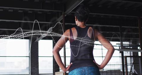 Standing athletic woman in loft gym wearing racerback tank and leggings, waveform overlay