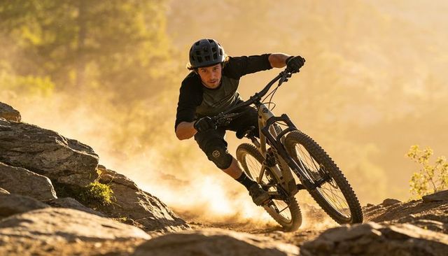 Mountain biker carving steep rocky downhill trail at golden hour with dust plume, fast