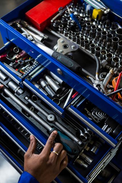 Mechanic selecting tools from a well-organized blue toolbox in a repair garage. Ideal for use in content related to automotive repair, mechanical work, tool organization, professional workshops, and maintenance services.