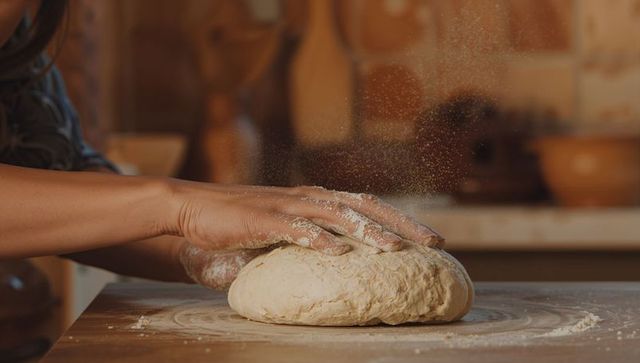 Kneading rustic bread dough on wooden countertop with flour dust and warm artisan light