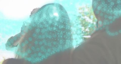 Backlit speaker presenting to silhouette audience with teal particle overlay