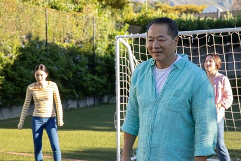 Happy family excitedly playing soccer outdoors on sunny day