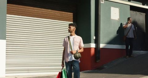 Diverse men pausing outside closed storefront holding shopping bags under urban sunlight