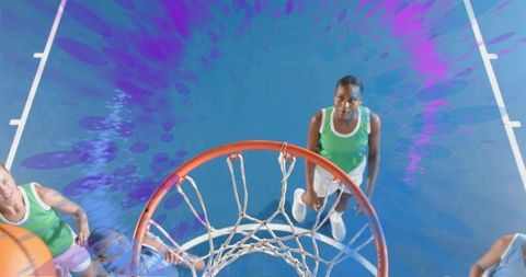 Overhead view jumping black female basketball player reaching rim on vibrant blue court
