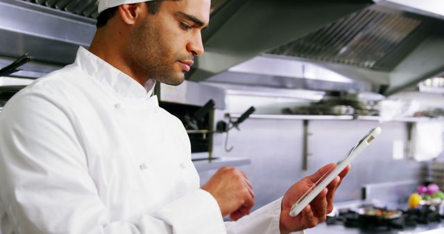 Chef using digital tablet in a professional kitchen. Perfect for articles on culinary innovation, restaurant management, tech use in cooking, and modern culinary techniques.