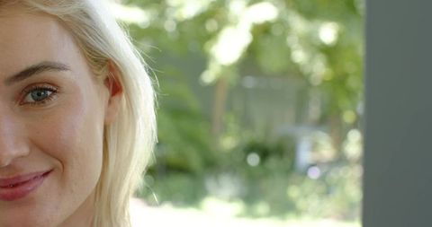 Blonde woman smiling in doorway, gazing at sunlit garden with soft bokeh background