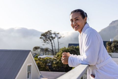 Asian woman enjoying morning on balcony in white bathrobe holding mug amid mountain mist