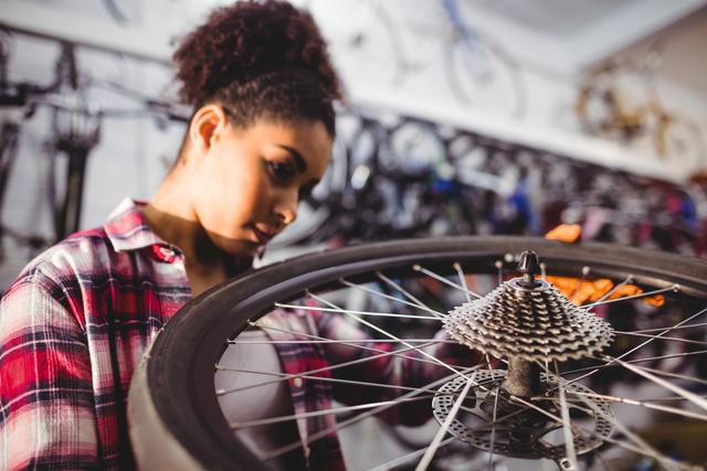 Mechanic examining a bicycle wheel, concentrating on repairing and maintaining the gear system in a workshop filled with bikes. This can be used for articles or content related to bicycle maintenance, repair shops, cycling enthusiasts, and hands-on work.